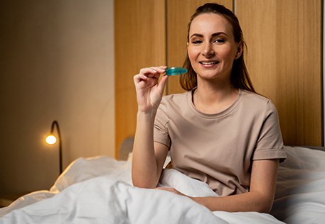 a woman sitting up in bed holding an oral appliance