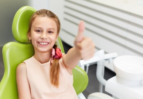 Child in dental chair giving thumbs up