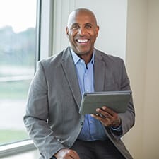 A middle-aged businessman holding a tablet and showing off his new dental implants