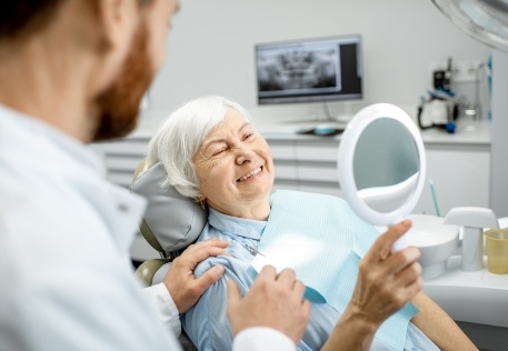 Woman looking at her smile after dental implant supported denture placement