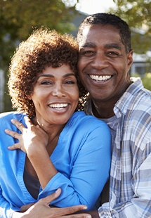 Older couple smiling after tooth replacement with dental implants