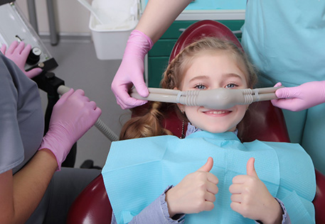 a child with a nose mask on in a dental treatment chair with their thumbs up