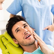 Young man in dental chair holding cheek