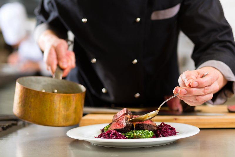 A chef pouring sauce onto a juicy steak.