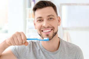 Man in grey using brushing tips from dentist in Dallas