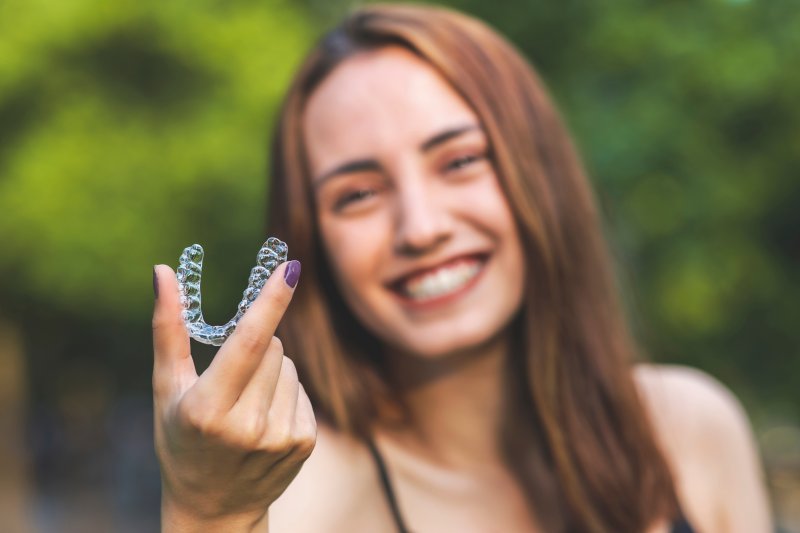 young girl smiling and holding an Invisalign aligner