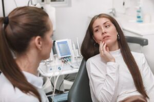 Patient in dentist’s chair holding mouth in pain and talking to dentist.